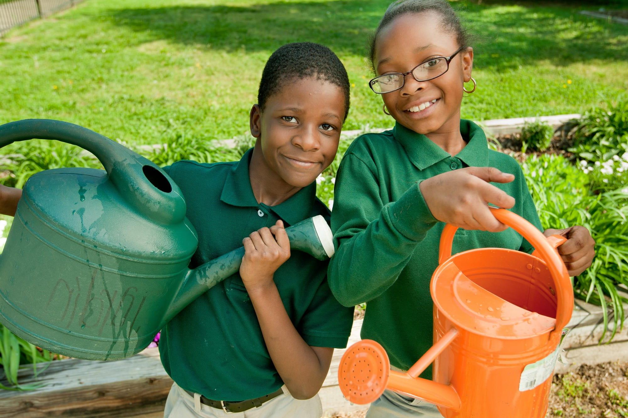 Two students holding watering cans as they participate in school garden program