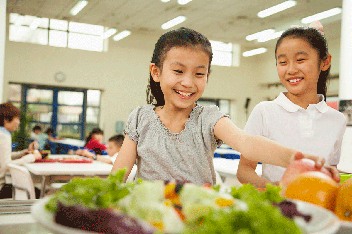 happy elementary students choose food in school lunch line
